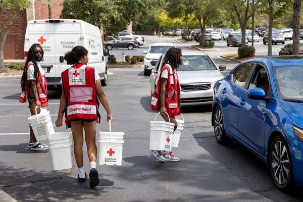 Three Volunteers carrying Red Cross buckets